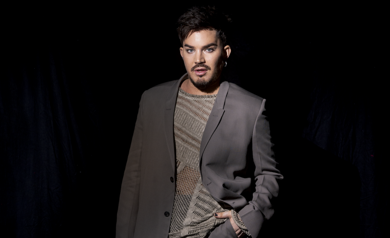 Adam Lambert wears a grey blazer and poses in a press shot