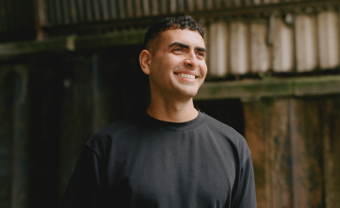 Sammy Virji poses in a black top in front of a dishevelled backdrop