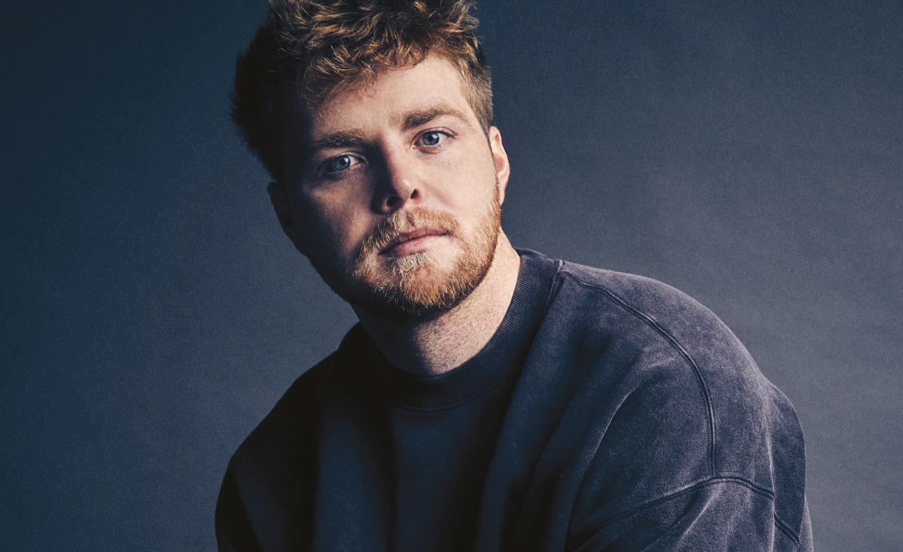 Alex Warren poses in a press hot wearing a navy jumper